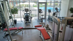 A gym with various exercise equipment, large windows, and a view of an outdoor swimming pool. - Fantastay Blvd Crescent (Dubai)