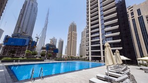 A rooftop swimming pool with lounge chairs and umbrellas, surrounded by high-rise buildings. - Fantastay Blvd Crescent (Dubai)