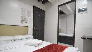 Ein Hotelzimmer mit einem Bett, einer roten Decke, einem weißen Kopfkissen, einem Telefon und einem Spiegel.