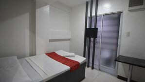 Ein Hotelzimmer mit Bett, einem an der Wand montierten Fernseher und einer Schiebetür.