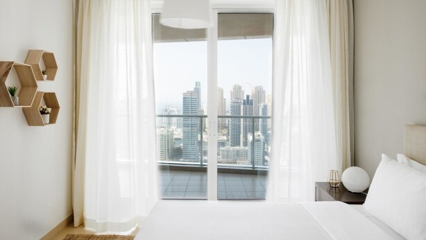 A modern hotel room with a large bed, a view of the cityscape through floor-to-ceiling windows, and a minimalist decor style. - Fantastay Laguna Tower (Dubai)