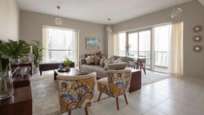 A spacious living room with a sofa, two patterned armchairs, a coffee table, and a dining area. Large windows provide ample natural light. - Fantastay Marina Tower (Dubai)