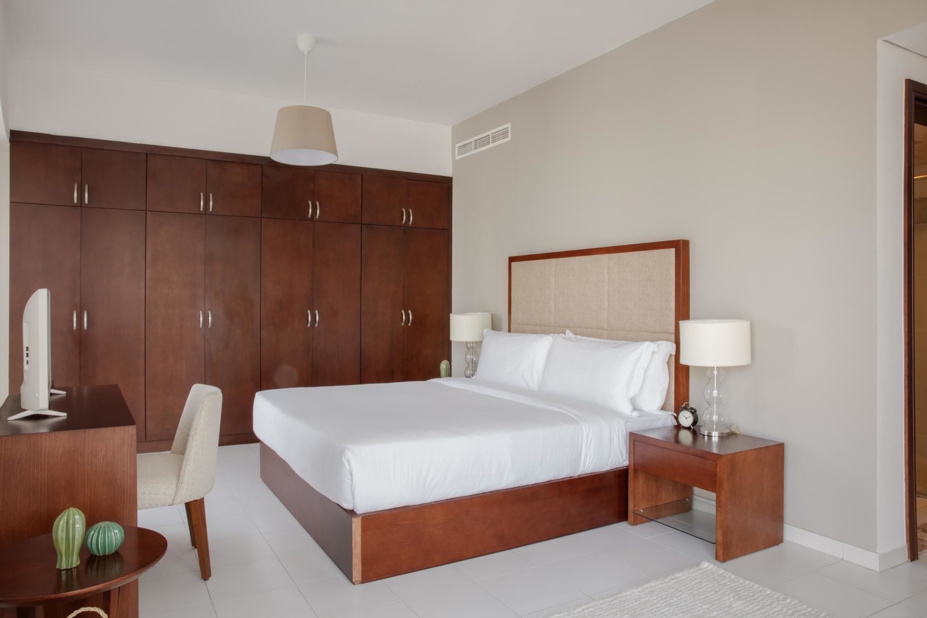 Moderni hotellihuone, jossa on suuri sänky, puinen vaatekaappi, yöpöydät ja työpöytä tuolilla.