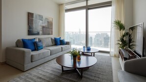 A modern living room with a grey sofa, blue cushions, a coffee table, and a large window offering a city view. - Fantastay Marina Gate Tower (Dubai)