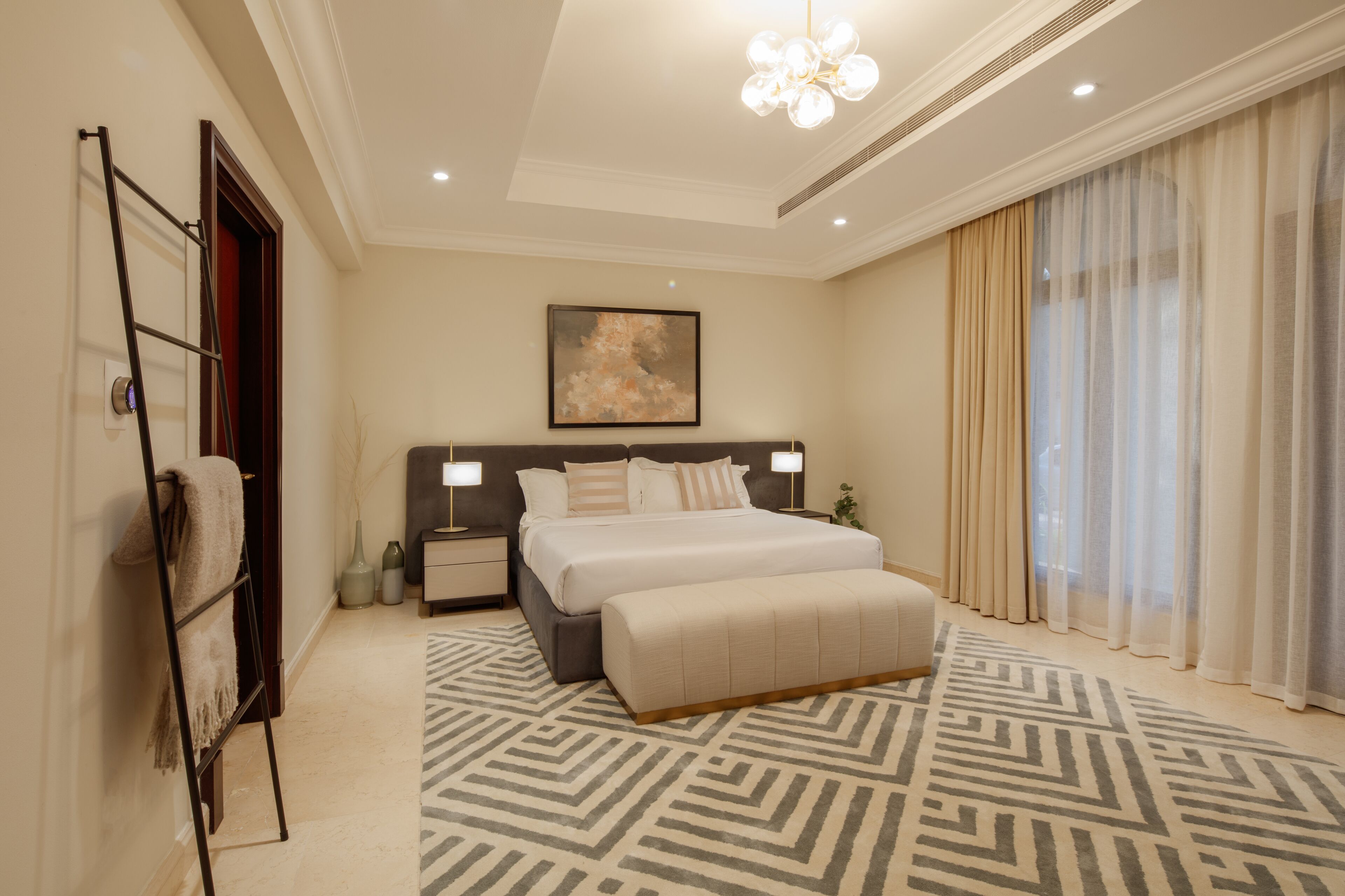 A modern hotel room with a large bed, bedside lamps, a patterned rug, and a large window with curtains.