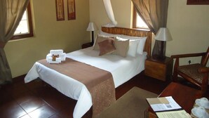 A hotel room with a bed, two bedside lamps, a chair, a small table with a tray of items, and a window with curtains. - Phokoje Bush Lodge (Selebi-Phikwe)