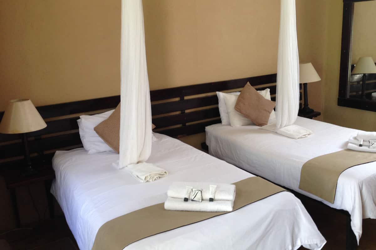 Deux lits d’hôtel avec du linge de lit blanc, une tête de lit en bois et un baldaquin.