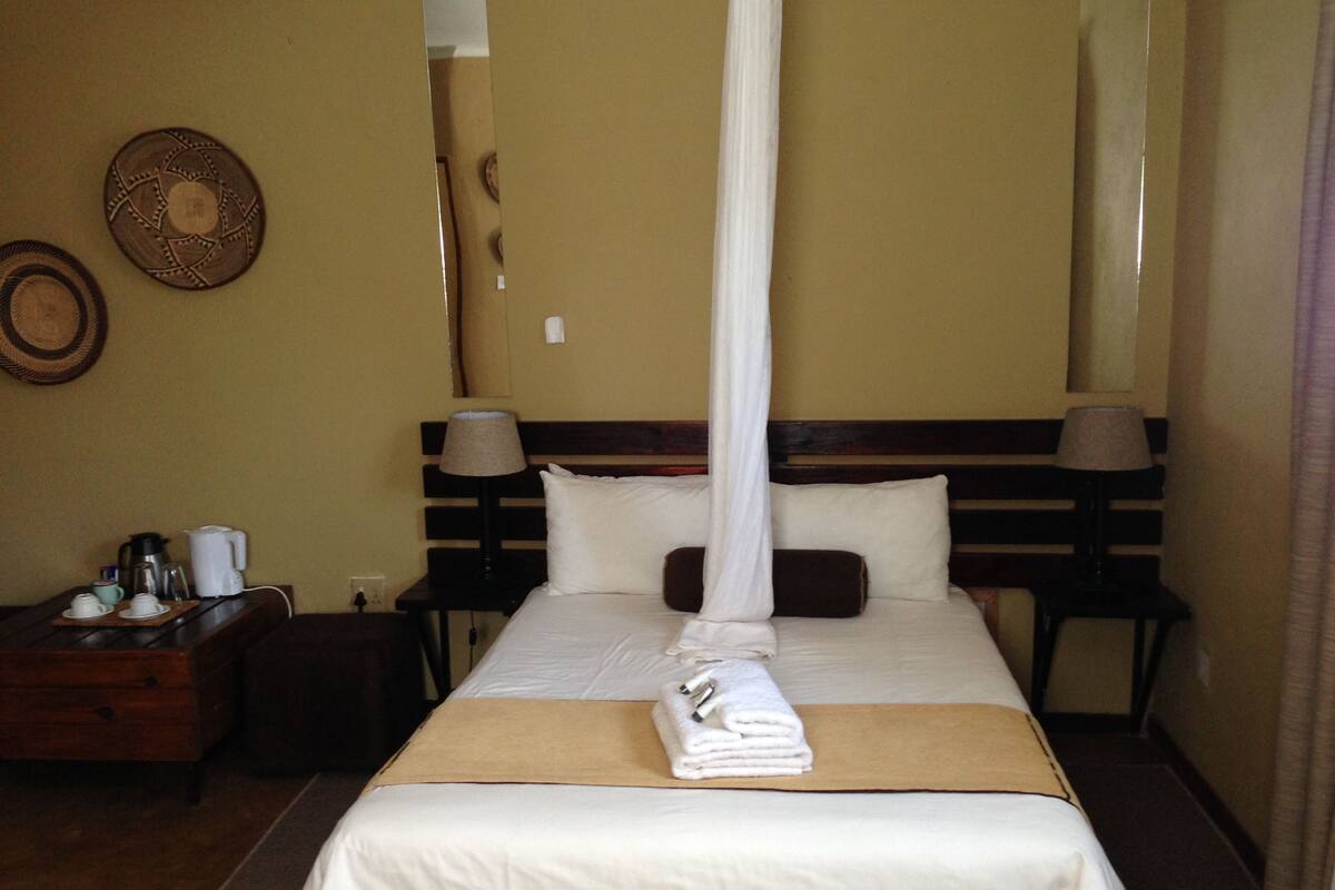 Une chambre d’hôtel comprenant un lit, des tables de chevet, une commode, une lampe et un élément décoratif mural.