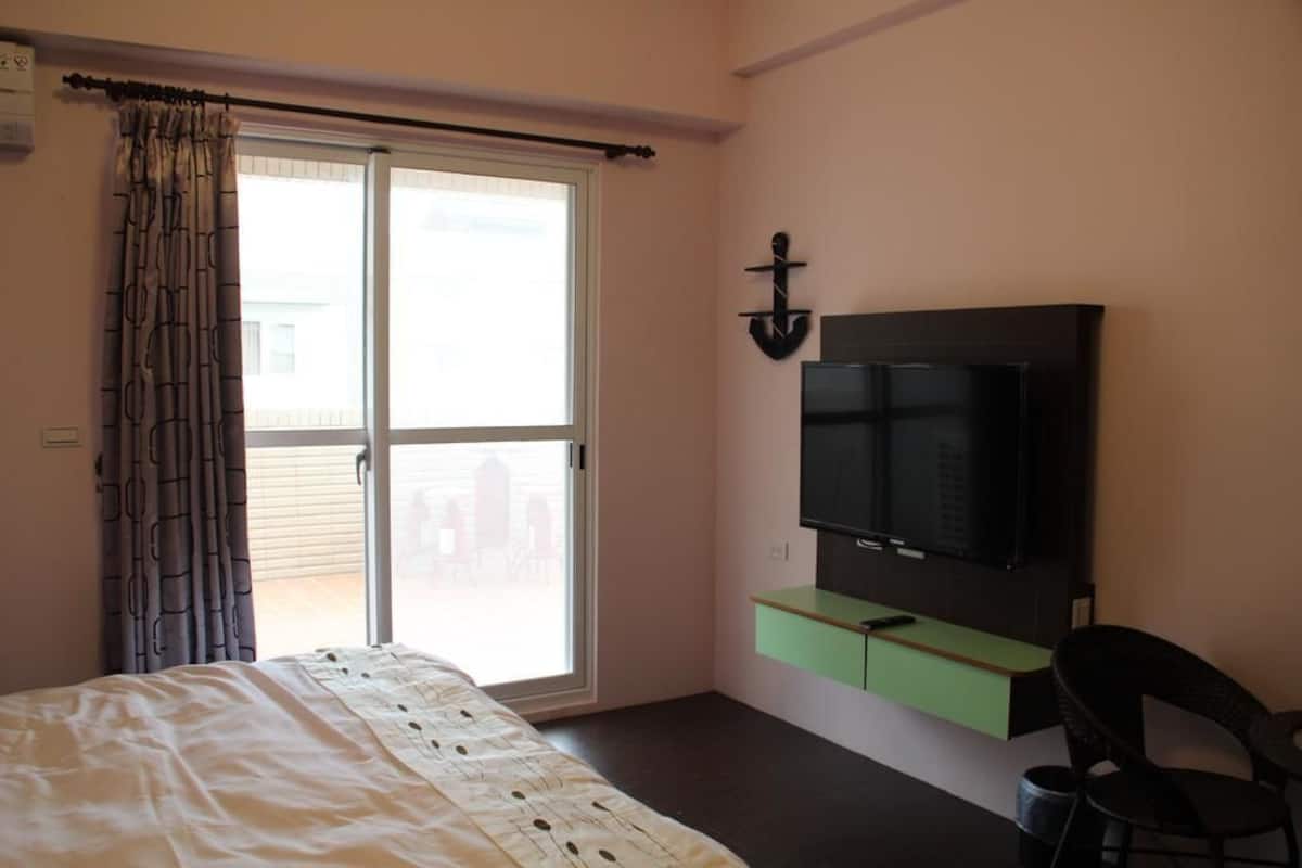 A bedroom with a bed, a TV mounted on the wall, a sliding glass door, and a chair.
