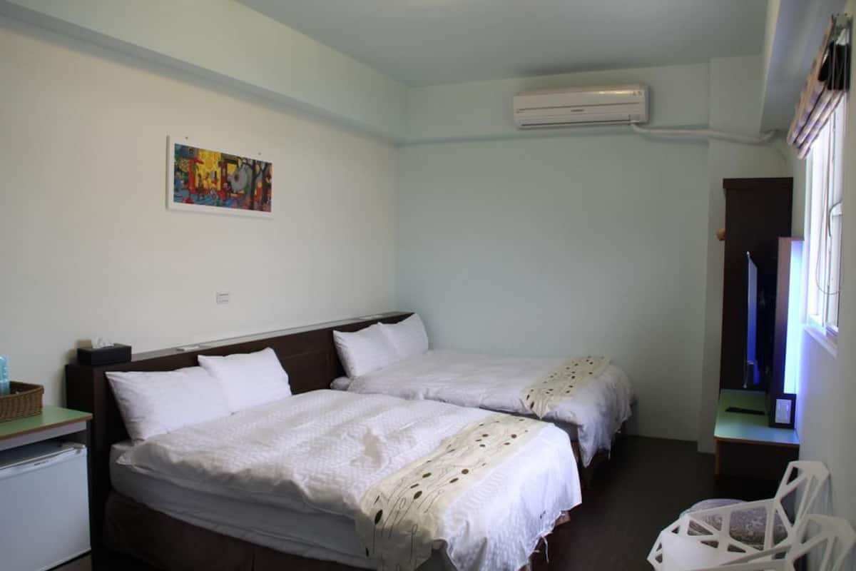 A hotel room with two beds, a small desk, a chair, and an air conditioning unit.