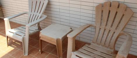 Dos sillas Adirondack de madera y una pequeña mesa frente a una pared de azulejos.