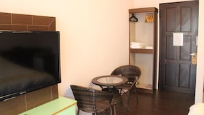 Habitación de hotel con televisión de pantalla plana, sillas de mimbre, una mesita, armario y puerta.