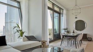 Un salon moderne comprenant un canapé, une table basse ronde en verre, un coin repas avec une table et des chaises, et de grandes fenêtres offrant une vue sur la ville.
