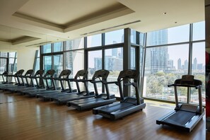 A gym with multiple treadmills aligned in rows, large windows, and a cityscape view.