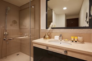 A modern bathroom with a glass-enclosed shower, a beige vanity with a gold vase, and toiletries on the counter.