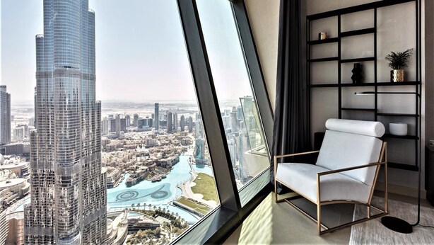 Un immeuble de grande hauteur offrant une vue sur le paysage urbain, avec un intérieur moderne comprenant une chaise blanche et une bibliothèque noire.
