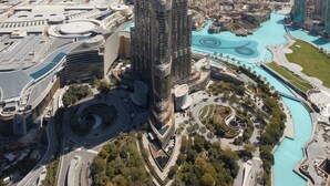 Un immeuble de grande hauteur doté d’une façade moderne en verre, entouré d’un espace paysager agrémenté de sentiers et d’éléments aquatiques.