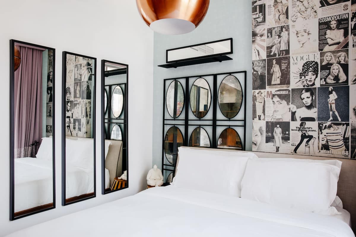 A hotel room with a large bed, multiple mirrors, and a wall decorated with vintage magazine clippings.