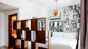A modern bedroom with a wooden shelf unit, a bed with white bedding, and a wall decorated with magazine-style photos. - FantaStay Claren Tower 1 (Dubai)