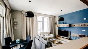 A modern living room with a sofa, TV, and dining area. - FantaStay Claren Tower 1 (Dubai)