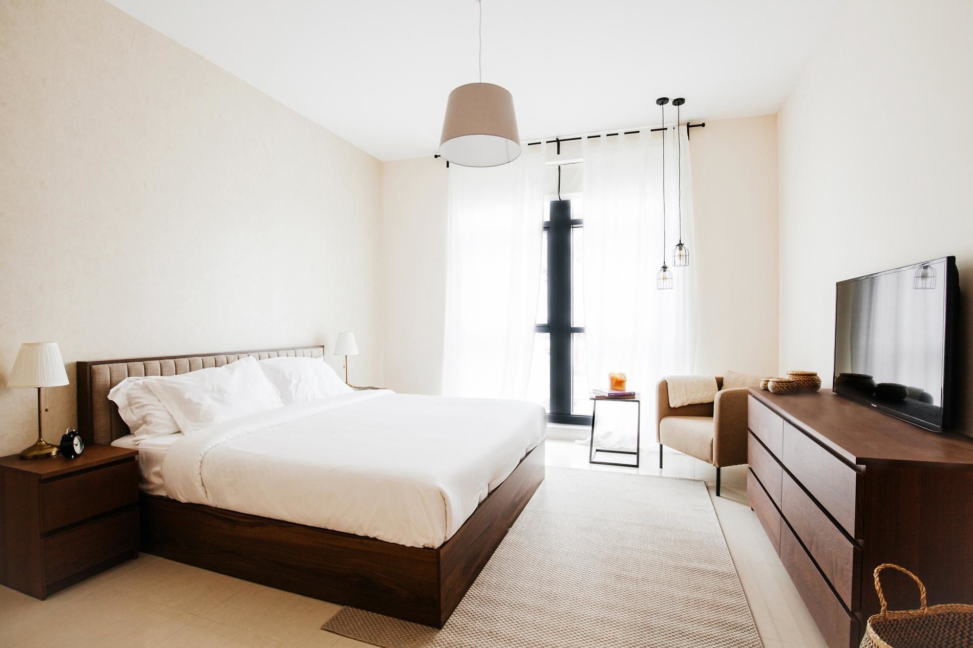 A modern hotel room with a large bed, bedside tables, a TV, and a view of the city.