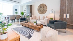 A modern living room with a sofa, coffee table, and a dining area with chairs and a table. - FantaStay Botanica Towers (Dubai)
