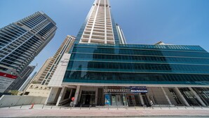 A modern building with a glass facade, a supermarket, and a medical center. - FantaStay Botanica Towers (Dubai)