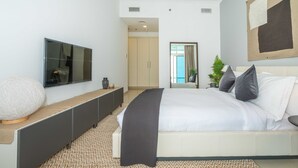 A modern bedroom with a large bed, a TV mounted on the wall, a console table, and a patterned rug. - FantaStay Botanica Towers (Dubai)