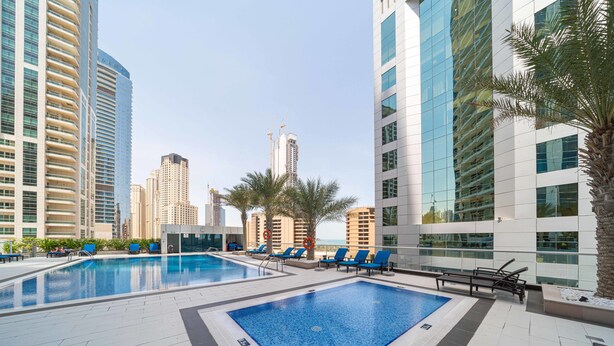 A rooftop swimming pool with lounge chairs and palm trees, surrounded by high-rise buildings. - FantaStay Botanica Towers (Dubai)
