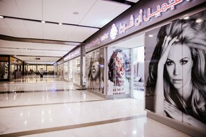 A modern shopping mall corridor with a Beauty Center featuring large promotional posters. - Fantastay Central Park Towers DIFC (Dubai)