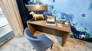 Una habitación con un escritorio de madera, una computadora portátil, una silla azul, una lámpara y un mural en la pared que representa una escena submarina.