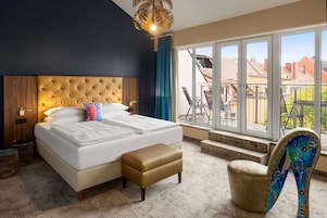 Een hotelkamer met een groot bed, een bankje, een stoel en uitzicht op het omliggende landschap.
