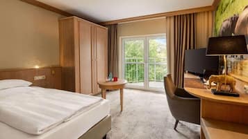 Habitación de hotel con cama, escritorio, silla, televisor y balcón con vistas a zonas verdes.