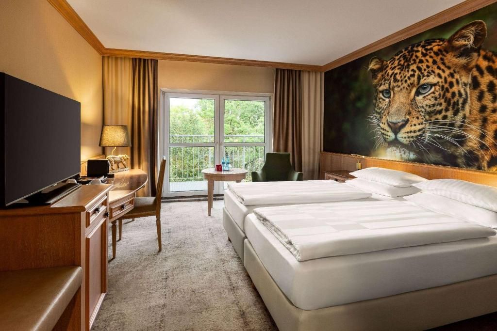 Habitación de hotel con un cuadro grande de un leopardo, dos camas, un escritorio con televisor y vistas por una ventana.