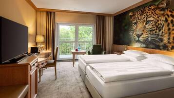 Habitación de hotel con un cuadro grande de un leopardo, dos camas, un escritorio con televisor y vistas por una ventana.