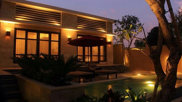 A modern building with a pool, outdoor seating, and a well-lit facade. - Kubu Kulat Villa (Pecatu)