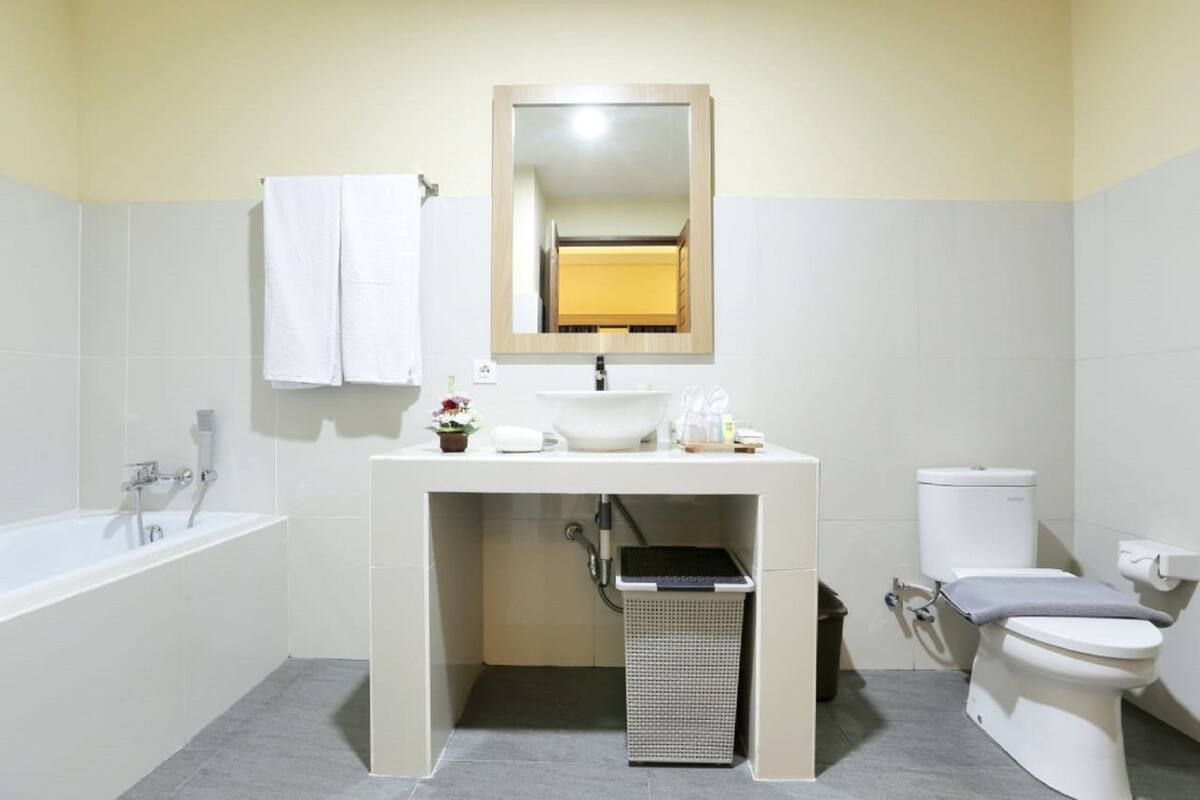 A bathroom with a bathtub, sink, mirror, toilet, and a trash bin.