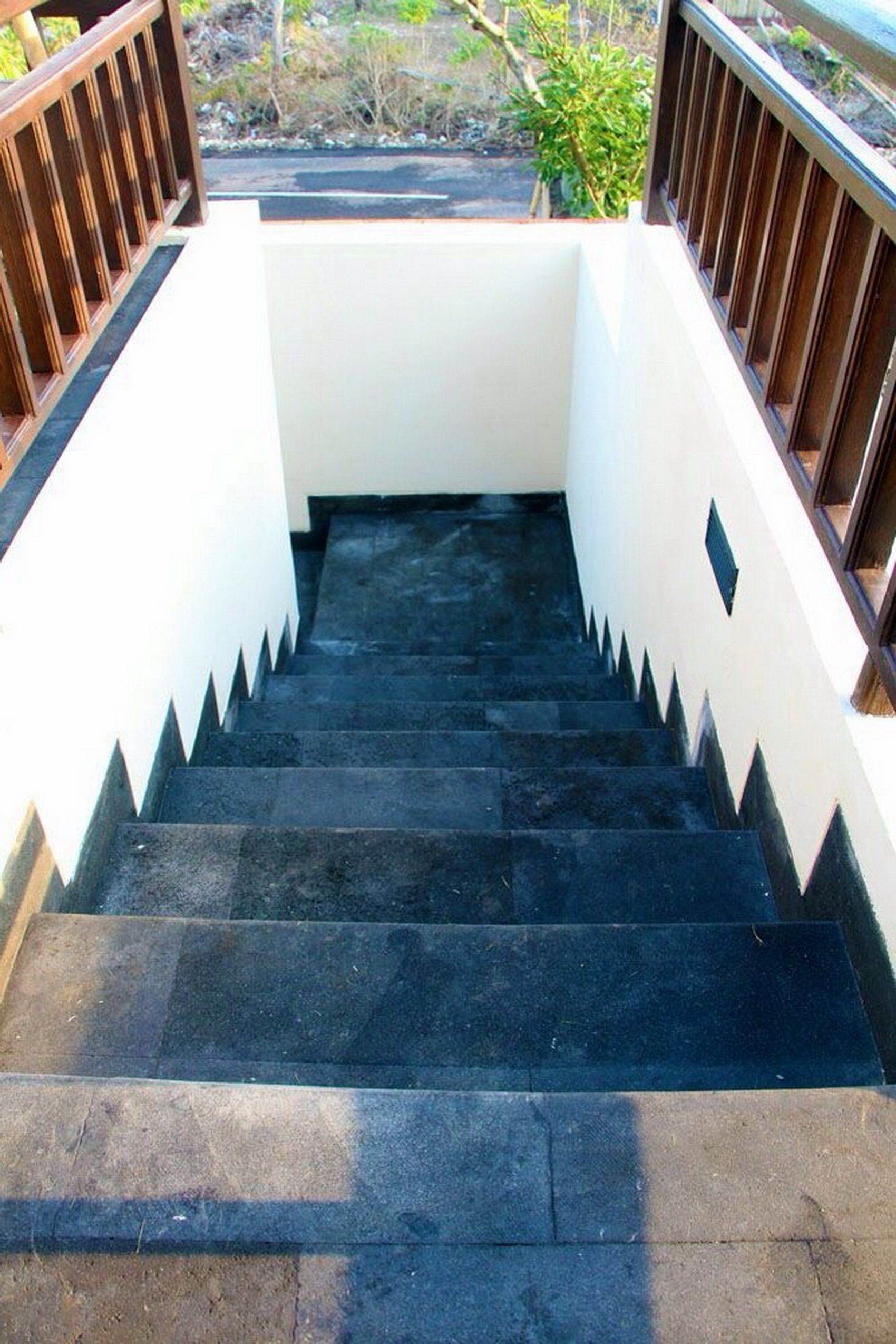 A staircase with black steps leading to a landing, surrounded by white walls and a wooden railing.