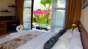 A hotel room with a bed, a desk, and a view of a pool and garden. - Kubu Kulat Villa (Pecatu)