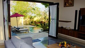 A modern living room with a glass door leading to a pool area. - Kubu Kulat Villa (Pecatu)
