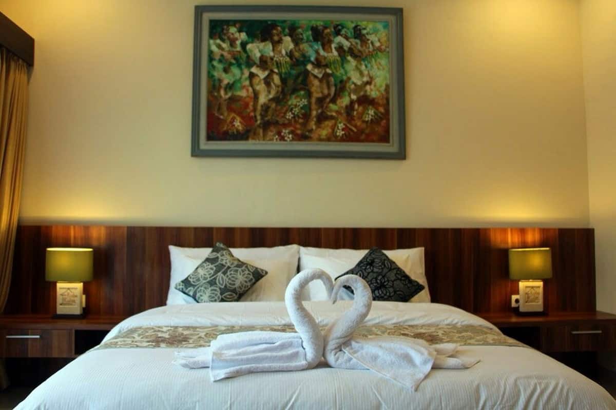 A hotel room with a bed, two nightstands, a painting on the wall, and towels arranged in a swan shape.
