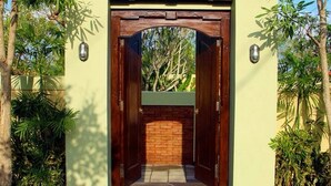 A modern entrance with a wooden door and brick wall, surrounded by lush greenery. - Kubu Kulat Villa (Pecatu)
