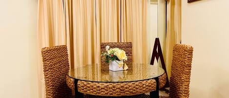 Un comedor con una mesa redonda de vidrio, sillas de mimbre y un jarrón de flores.