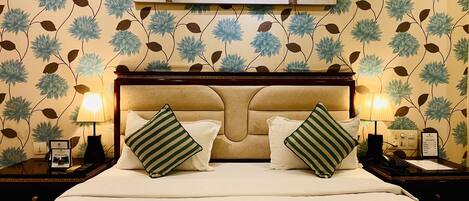 A hotel room with a large bed, two nightstands, a lamp, and a floral wallpaper pattern.