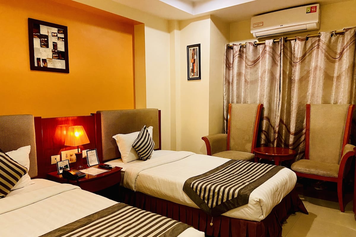 A hotel room with two beds, a desk with a lamp, a chair, and a window with curtains.
