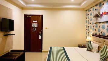 A hotel room with a bed, a television mounted on the wall, a ceiling fan, and a door with a sign.