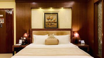 A hotel room with a large bed, two bedside tables with lamps, a framed picture above the bed, and a wooden door.