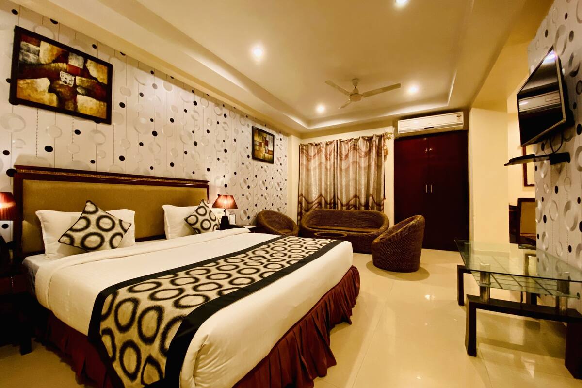 A hotel room with a large bed, a desk, a chair, a TV, and a ceiling fan.