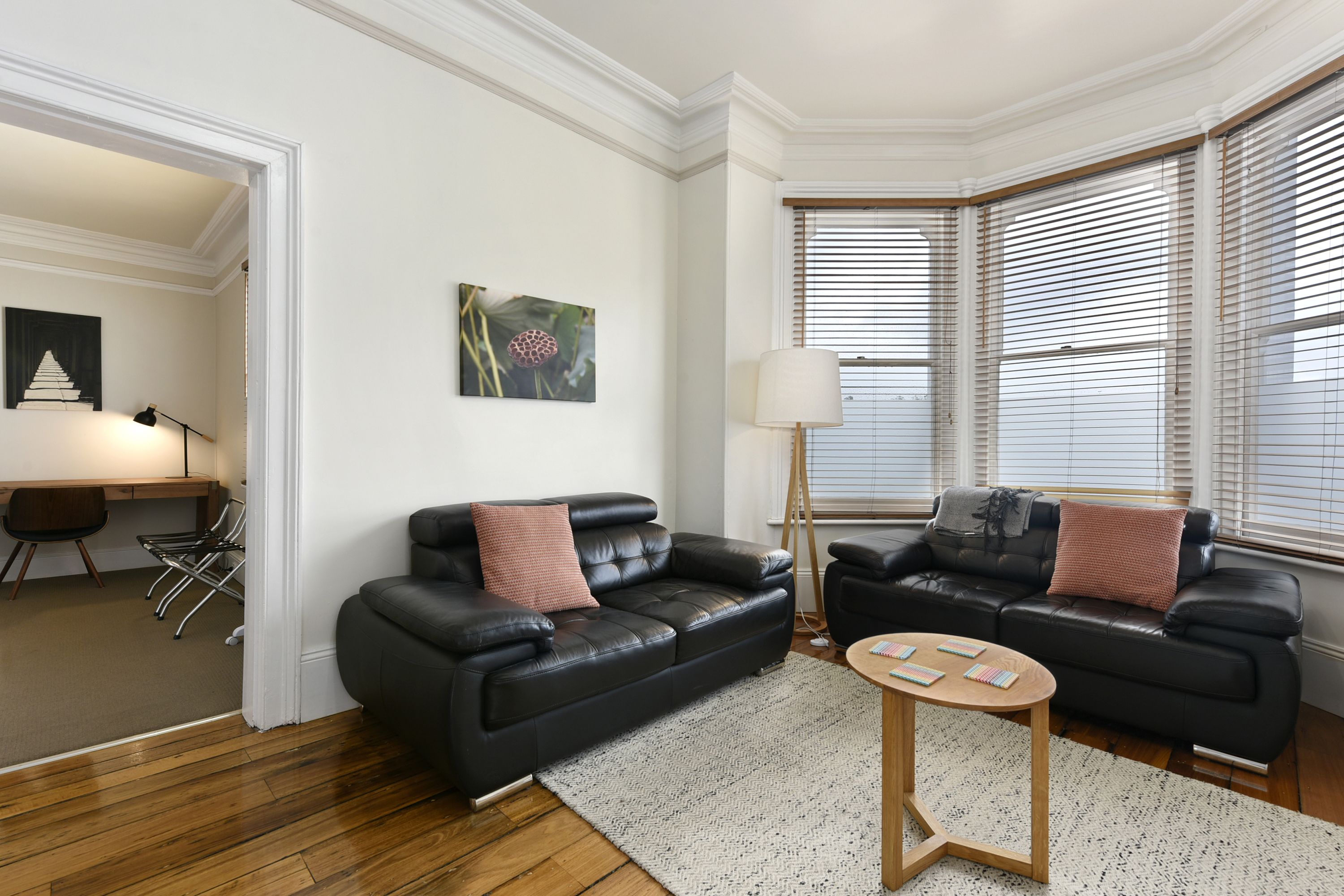A modern living room with two black leather sofas, a wooden coffee table, and a white rug.