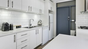 A modern kitchen with white cabinetry, stainless steel appliances, and a grey door. - Trinity Hill Apartments (Hobart)
